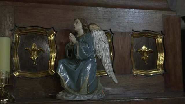 A serene angel statue in prayer, set against dark wood with golden fleur-de-lis symbols, exuding a sense of peace and reverence within a sacred space.