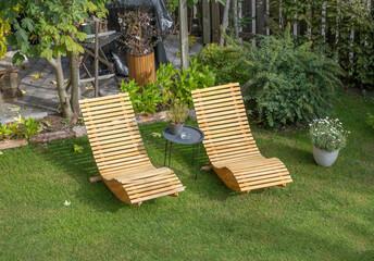Two wooden deck chairs on the lawn in the backyard of a house