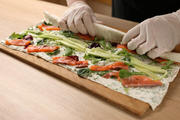 Lavash with filling is wrapped in a roll. Preparation of a roll with cheese, fish and vegetables
