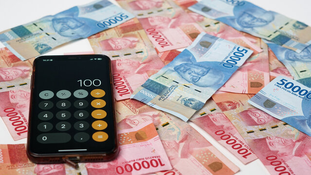 photo of a smartphone calculator and a collection of rupiah banknotes on a white background