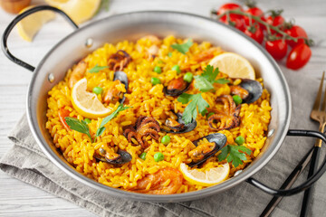 Traditional spanish seafood paella with rice, mussels, shrimps in a pan on wooden background.