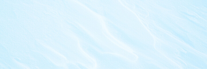 Wide panoramic winter background with snowy ground. Natural snow texture. Wind sculpted patterns on snow surface.