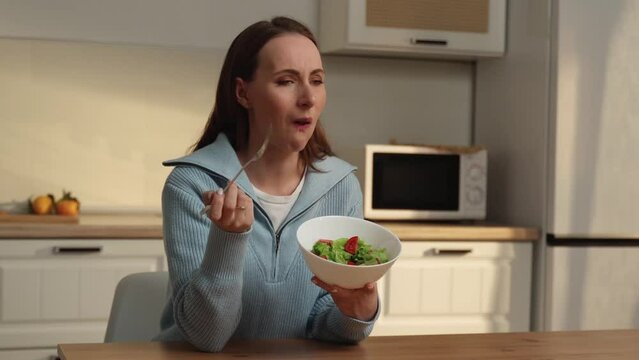 Lack of appetite. An unhappy woman holds a fork with a green salad while sitting in the kitchen. Loss of taste and smell. 