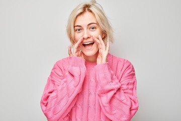 Portrait of blonde girl shouting loudly with hands, news, palms folded like megaphone isolated on...