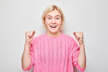 Portrait of smiling face blond young woman clenching fists and rejoicing, celebrating victory...