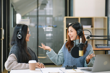 Asian woman use microphones wear headphones with laptop record podcast interview for radio. Content...