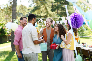 Garden birthday party with surprise. Friends holding birthday gifts and flowers. Family garden gathering during warm autumn day.