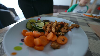 Adding pieces of chicken into healthy plate of carrots and zucchini for lunch