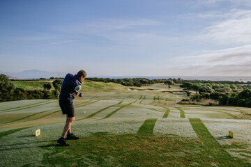 Sotogrande, Spain - January, 23, 2024 - A golfer in mid-swing on a course overlooking a coastal...
