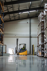 Side view of forklift in warehouse with male driver. Warehouse worker preparing products for...
