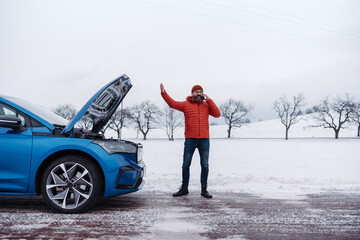 Angry man standing by electric car, battery run out of power before reaching destination. Man phone...