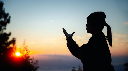 Silhouette of christian woman prayer on sunset background. Woman raising his hands in worship for...