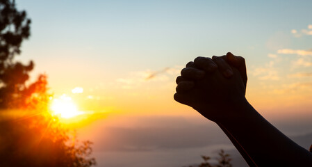 Silhouette of christian woman prayer on sunset background. Woman raising his hands in worship for...