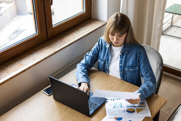 Modern young business woman freelancer working using laptop, engaged in remote work sitting at home at the table