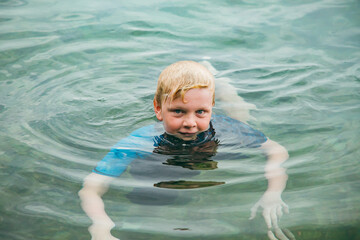 Blonde boy swimming with head just above water in clear saltwater pool on holiday in Newcastle