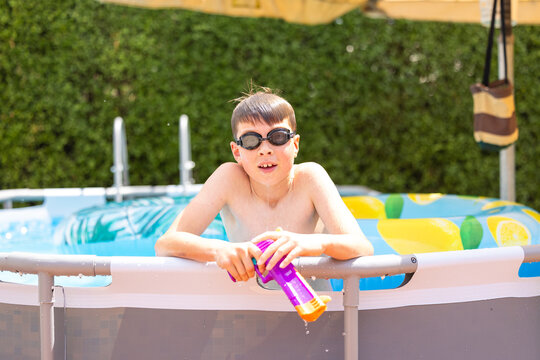 Boy swimming in backyard pool with water pistol on summer day