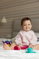 happy cute little child girl playing and pretending drinking tea from toy cups on bed