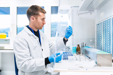 Lab technician carefully inspects the contents of a test tube against the light in a clean,...
