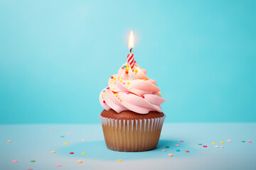 Cupcake with pink frosting, sugar sprinkles and burning birthday candle in front of blue background