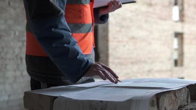 A construction engineer is looking at working drawings of a high-rise building. Project management officer, inspector, architect checking the scope of work at the construction site.