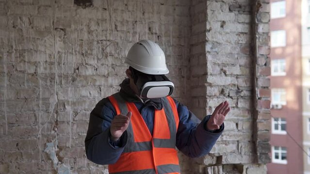 An architect-builder wearing virtual reality glasses walks around a construction site. Moves digital virtual objects with his hands, looks at the characteristics of the transmitted glasses. 
