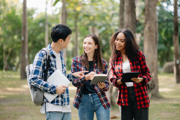 Three young college students is reading a book while relaxing sitting on grass in a campus park with her friends. Education concept