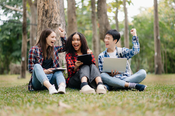 Three young college students is reading a book while relaxing sitting on grass in a campus park with her friends. Education concept