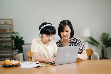 Homeschool Asian young little boy learning online and does homework by using computer and tablet with mother help, teach and encourage. son smile to study at home together with mom