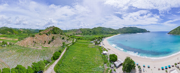 Panoramic Aerial view of paradise beach of white sand and crystal clear waters next to the countryside with mountains in the distance in Lombok, indonesia. 