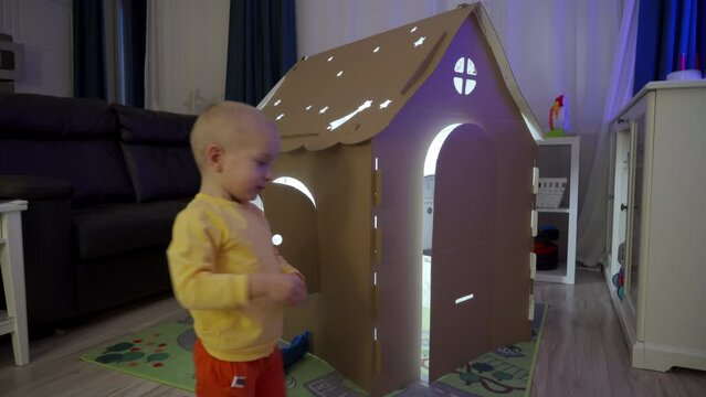 3-year-old child playing with house cardboard coloring playhouse, little boy drawing on wall of carton house toy for children, kid having fun at home.