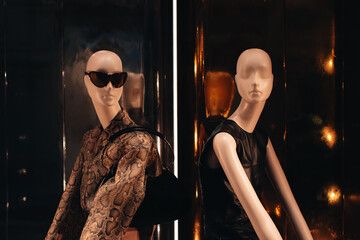 Mannequins in a boutique window dressed in a black dress and a leather jacket with a snake print
