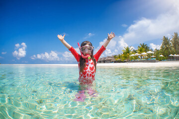 A happy girl in snorkeling gear enjoys the emerald water of the tropical Indian Ocean, Maldives...