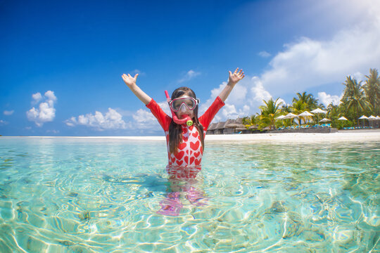 A happy girl in snorkeling gear enjoys the emerald water of the tropical Indian Ocean, Maldives islands