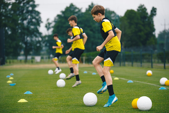 Football Academy For Teens. Youth Football Player in Soccer Ball Control Drills. Young Boys in the Football Team At Workout. Ambitious Young Athletes Improving Skills and Jumping Over Hurdles