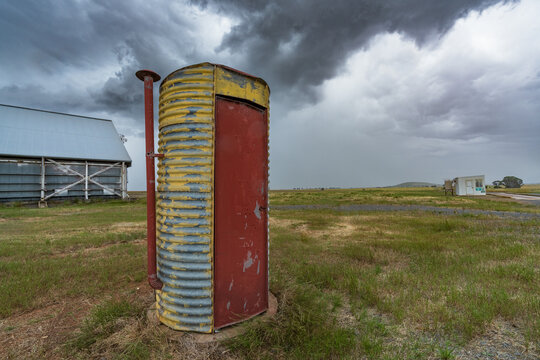 A corrugated iron toilet in the middle of farmland with dramatic clouds overhead