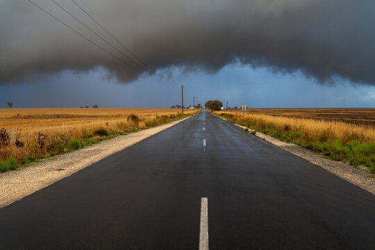 Rain falling from a dramatic stormfront over a long straight country road