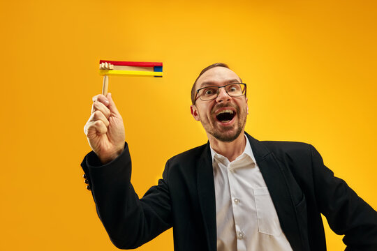 Jewish man in his 30s, in glasses, yarmulke joyfully posing with wooden noisemaker, gragger against yellow studio background. Concept of Purim holiday, Jewish traditions, history and culture
