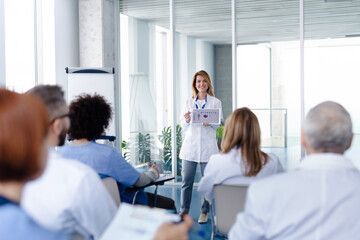 Female doctor as speaker at conference for healtcare workers, medical team sitting and listening presenter. Medical experts attending an education event, seminar in board room. - obrazy, fototapety, plakaty