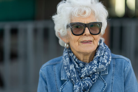 head and shoulders of elderly white-haired lady wearing denim with sunglasses and a scarf