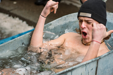 Handsome boy wearing a hat ice bathing in the cold water among ice cubes in a vintage bathtub. Wim...