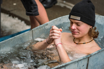 Handsome boy wearing a hat ice bathing in the cold water among ice cubes in a vintage bathtub. Wim...