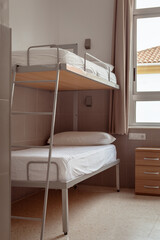 A clean and minimalistic hostel room with a bunk bed, white bedding, and a small wooden bedside...