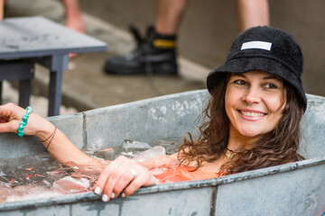 Pretty girl or woman wearing a hat, smiling and ice bathing in the cold water among ice cubes in a...