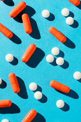 White tablet pills and orange capsules on blue background