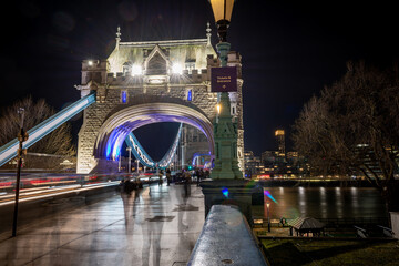 Obraz premium A night time, long exposure shot on Tower Bridge with pedestrian, tourists visiting this iconic landmark and light trails from passing vehicles.
