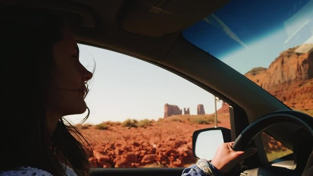 Smiling happy young woman with flying hair driving along scenic desert mountain road at Monuments Valley, Arizona.