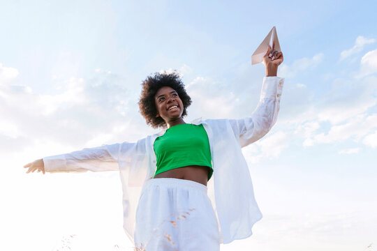Cheerful woman playing with paper plane in field