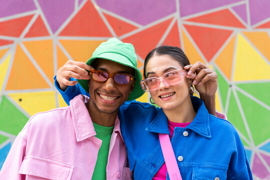 Smiling couple holding sunglasses in front of colorful wall