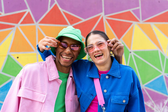 Cheerful couple holding sunglasses in front of colorful wall
