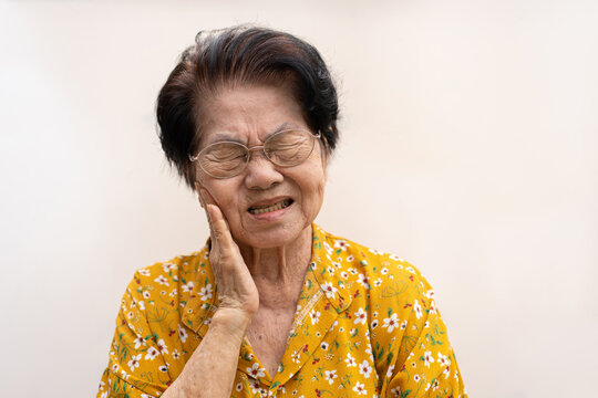 Asia old senior woman suffering from severe toothache, holding her cheek and suffering strong dental pain on white background, tooth decay, tooth sensitivity, oral health care concept.